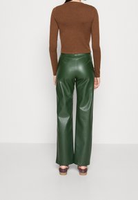 Brązowa dopasowana bluzka z długim rękawem połączona z zielonymi szerokimi spodniami z ekoskóry o wysokim stanie, ukazującymi gładką teksturę i proste linie.