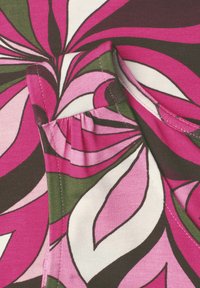 Tissu rose vif, vert, blanc et marron avec des motifs audacieux en forme de feuilles tourbillonnantes et des coutures visibles en gros plan.