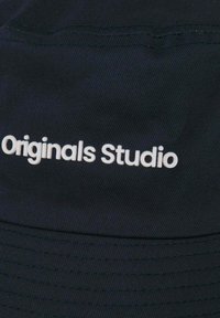 Zwarte pet van een gestructureerde stof met de tekst "Originals Studio" in het wit, gecentreerd op het voorpaneel.