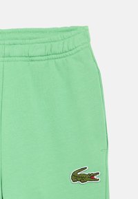 Πράσινη βαμβακερή φόρμα με ελαστική μέση, με υφασμένο κροκοδειλάκι κέντημα στο αριστερό πόδι.