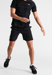 Černé sportovní tričko a šortky, lehká látka, základní design, kulatý výstřih a logo na hrudi. Černé tenisky s tkaničkami.