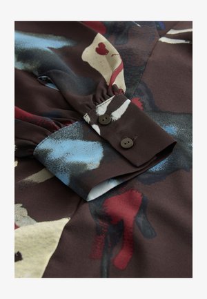 Sötét barna színű, hosszú ujjú blúz absztrakt mintákkal kék, piros és krémszínben. Gombos mandzsettával és összegyűrt ujjrészlettel rendelkezik.