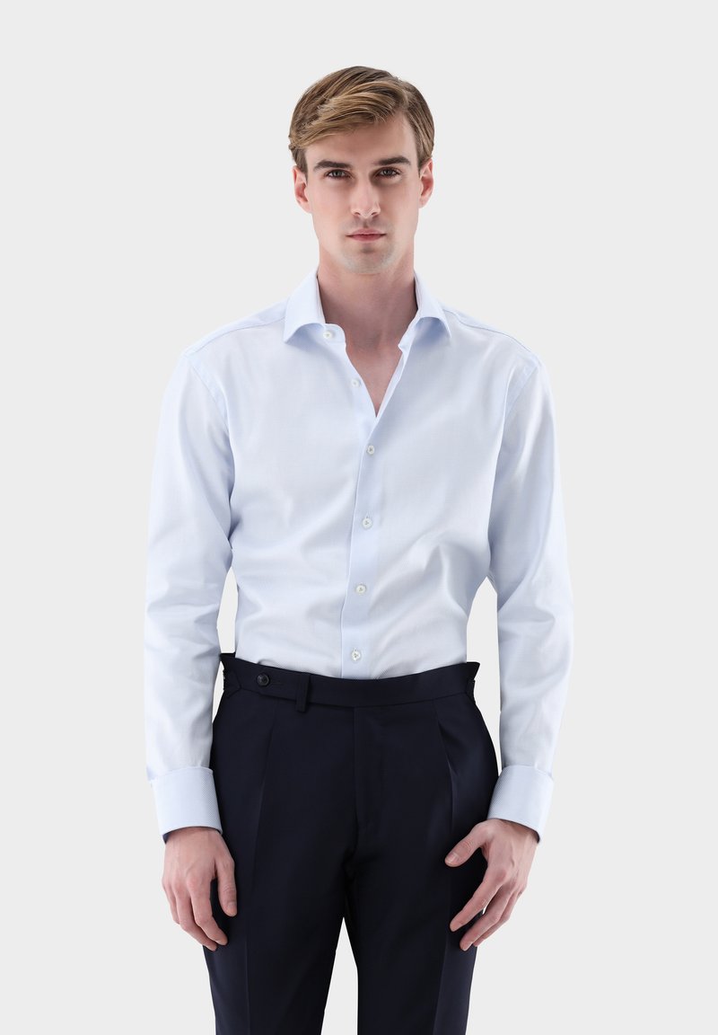 Chemise habillée bleu clair à carreaux avec col à pointes écartées et manches longues, associée à un pantalon sur mesure bleu marine foncé. Détail boutonné sur le devant.