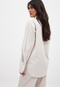 Striped button-up shirt in light beige and white. Features long sleeves, a spread collar, and a curved hem for a relaxed fit.