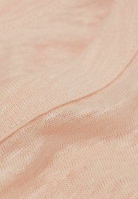 Ljusrosa stickad tyg, mjuk textur, med en lös väv och subtilt mönster, med en slät kant längs kanten.