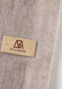Felt fabric in muted beige with soft texture; attached leather tag branded "BELLEMERE NEW YORK" in brown. Features two small holes for attachment.