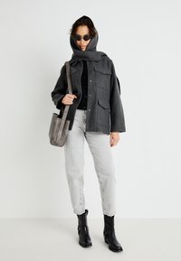Giacca grigia in misto lana con cappuccio, chiusura a bottoni e tasche frontali. Abbinata con un maglione nero, jeans grigi chiari e stivaletti neri.