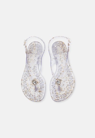 Sandales en gelée transparentes avec paillettes dorées, design à bride en T, bride de cheville réglable et accent rectangulaire en strass sur le dessus.
