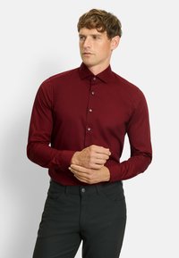 Bordeaux langarm overhemd met knopen en een puntkraag, gecombineerd met zwarte broek. Soepele stof, getailleerd ontwerp.