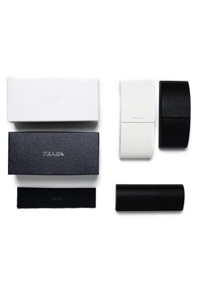 Deux étuis rectangulaires pour lunettes Prada, un blanc et un noir, avec des boîtes Prada assorties noire et blanche et un chiffon de nettoyage noir.