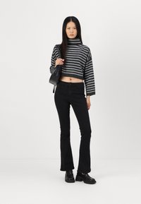 Maglione cropped a collo alto a righe grigio e nero, abbinato a jeans neri a zampa d'elefante e scarpe con piattaforma nere, mentre tiene in mano una piccola borsa nera.