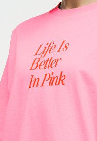 Άτομο που φοράει φωτεινό ροζ φούτερ με κόκκινο κείμενο στο στήθος που γράφει "Η ζωή είναι καλύτερη στο ροζ".