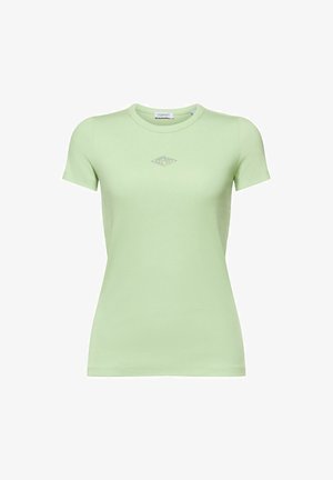 Abrigo ligero beige sobre una camiseta verde y una camisa a rayas. Pantalones blancos de pierna ancha y zapatillas beige completan el conjunto.