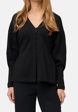 Femme portant un cardigan noir ample à col en V boutonné avec des manches longues et un pantalon noir assorti.