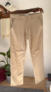 Calças bege claras feitas de um tecido suave, com bolsos frontais, fecho de botão e pernas retas, exibidas contra um fundo neutro.