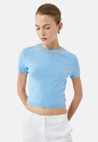 Suéter de manga corta azul claro con un cuello decorado con cuentas, hecho de un material de punto suave, con un dobladillo acanalado y un diseño ajustado.