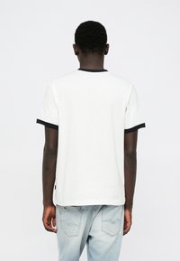 Άσπρο κοντομάνικο μπλουζάκι με μαύρο ριπ γιακά και μανσέτες, με άνετη εφαρμογή και διακριτικές λεπτομέρειες ραφής. Φορεμένο με ανοιχτόχρωμο μπλε τζιν.