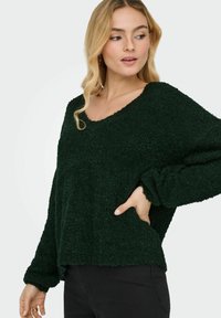 Grüner, strukturierten Pullover mit V-Ausschnitt, überschnittenen Schultern und langen Ärmeln. Besitzt einen lockeren Schnitt und ein weiches, gemütliches Material.