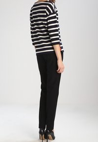Top a righe blu navy e bianche a maniche lunghe con scollatura rotonda, abbinato a pantaloni neri e scarpe con tacco, visto da dietro.