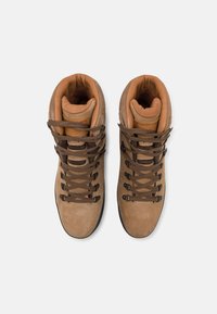 Brune suedes fjellsko med polstret krage, mørkebrune snørebånd og en strukturell gummisåle. Merkbar logo på tungen.