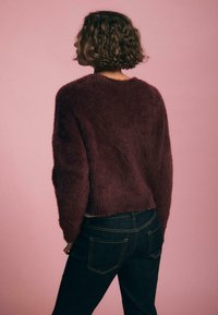 Burgunderfarbener, flauschiger Pullover mit lässiger Passform, rundem Halsausschnitt und langen Ärmeln, kombiniert mit dunkelblauen Jeans.