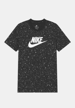 T-shirt noir à manches courtes avec un motif de taches blanches et un grand logo Nike blanc centré sur la poitrine.