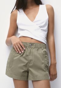 Haut blanc sans manches avec un col en V, associé à un short vert olive à taille élastique, doté de poches avant et d'une coupe décontractée.