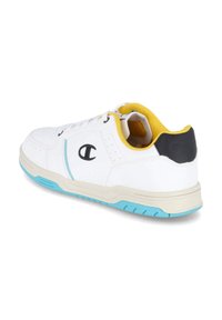 Weiße Sportschuhe mit blauen Sohlelementen, gelbem Innenfutter und schwarzer Ferse. Glattes Obermaterial mit Logodetails an der Seite.