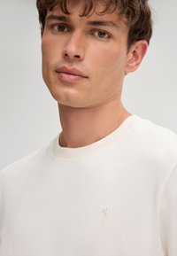 Witte crewneck sweatshirt van zacht materiaal, met een subtiele geborduurde logo op de borst en geribbelde halslijn en manchetten.