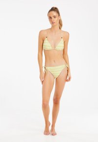 Geltona trikampė bikini kostiumo komplektas su vertikaliomis baltomis juostelėmis; prisiriša kaklo ir klubų srityse; švelni medžiaga; minimalistiškas dizainas be puošmenų.