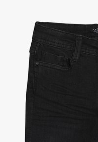 Černé džíny z denimu s úzkým střihem, standardním pasem, přední kapsou a černým kováním. Látka má hladkou texturu s jemným prošíváním.