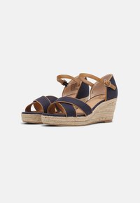 Sandali wedge in tela blu navy con cinturini beige e fibbia regolabile. Corda di juta in stile espadrille avvolta attorno al tacco a zeppa.