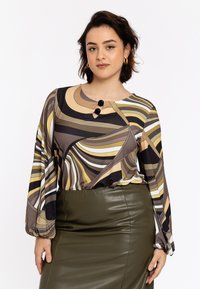 Langærmet bluse med abstrakte bølgemønstre i brun, creme og gul, med en rund halsudskæring og to sorte knapper. Kombineret med en mørkegrøn blyantskirt.