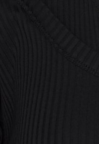 Schwarzer gerippter Stoff mit vertikalen Linien, im V-Ausschnitt-Design und dezenten Nähdetails, die ein strukturiertes Erscheinungsbild erzeugen.