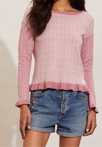 Pull en tricot rose clair avec des motifs circulaires, ourlet volanté et poignets à volants. Associé à un short en denim avec des étoiles brodées.