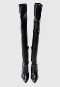 Fekete bőrből készült, combig érő csizma, hegyes orral, sima textúrával és oldalsó cipzárral a záródáshoz, a tetején megerősített varrással.