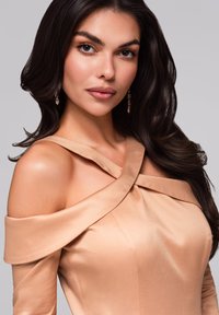Beige Satin-Kleid mit schulterfreiem Schnitt und Kreuzdekolleté; Modell trägt hängende Ohrringe; glatte Textur und figurbetonte Form.