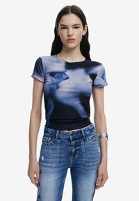 Sinine ja must lühikeste varrukatega ülikond, millel on tekstuuriga ribad ja abstraktne muster. Kombineeritud kulunud teksadega, millel on punased lillemustrid.