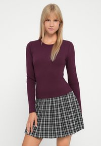 Purple ribbed long-sleeve top paired with a black and white plaid pleated skirt, featuring a fitted design and soft texture.