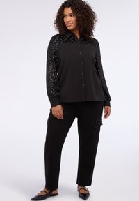 Czarna koszula na guziki z ramionami ozdobionymi cekinami, zestawiona z czarnymi spodniami bojówkami z teksturowanymi akcentami i luźnym krojem.