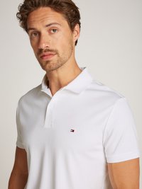 Witte polo gemaakt van katoen, met een geknopt kraag en een klein geborduurd logo in rood, wit en blauw op de borst.