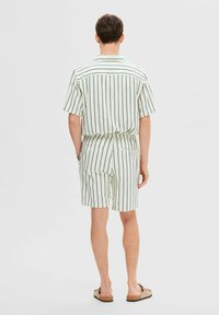 Trumpas rankovėmis marškiniai ir šortai iš lengvos medžiagos su žaliais vertikaliais dryžiais, turi laisvą siluetą ir nugarines kišenes.