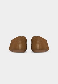 Paire de mocassins en daim marron sans lacets vus de dos sur un fond blanc uni.