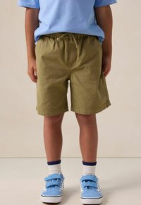 Shorts kaki en tissu léger, dotés d'une taille élastique avec cordon de serrage. Portés avec un tee-shirt bleu et des baskets bleues.
