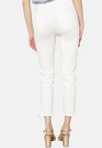 Witte enkel-lange jeans met een slim fit ontwerp, lichte stretch en achterzakken. Gecombineerd met gouden hoge hakken sandalen.