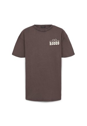 T-shirt en coton marron à manches courtes et col ras du cou. Présente le texte "RODEO" en blanc dans une police stylisée sur la partie gauche de la poitrine.