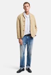 Beige Kordjacke mit Knöpfen, hellblau gestreiftes Hemd, hellblaue Jeans und schwarze Loafers. Das Outfit hat eine lockere Passform und einen lässigen Stil.