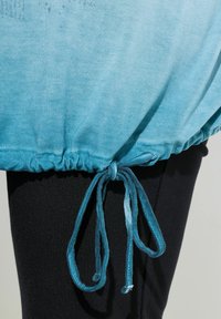 Blaues Stoffband, das zu einer Schleife über schwarzen Hosen gebunden ist, mit geraffter Naht entlang der Stoffkante.