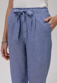 Light blue, textured trousers with a tie waist, featuring side pockets and subtle pleats for added style. Soft, breathable fabric.