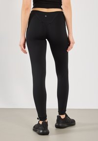 Svart leggings laget av elastisk stoff, med høy midje, tettsittende silhuett og en liten logodetalj på baksiden.
